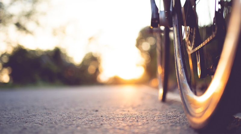 Close-up image of the wheels of a bicycle on a road with the sun shining behind them to support future of bicycles article