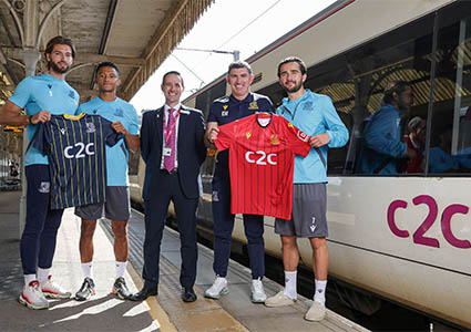 Footballers holding c2c sponsored shirts standing by a c2c train