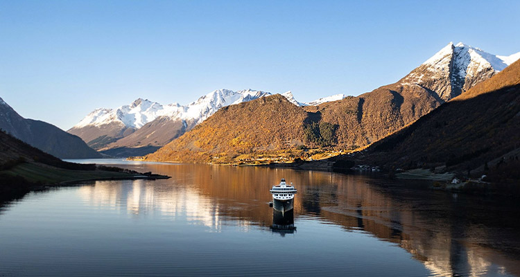 Cruise ship in a fjord with snow capped mountains in the background