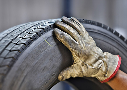 person's hand in a worn leather work glove inspecting a large, dark rubber tire