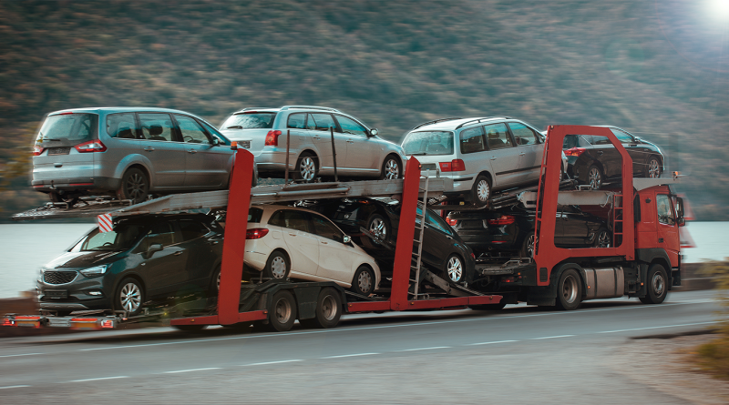 Car carrier truck transporting multiple vehicles on a highway during interstate auto shipping, with stacked cars on an open trailer in motion.