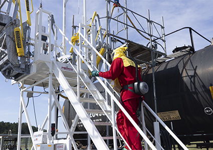 a worker in protective gear ascending a gangway system to access the top of a railcar