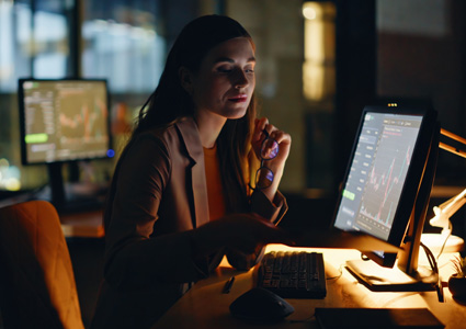 a professional in a dark office environment working with multiple computer screens displaying data charts