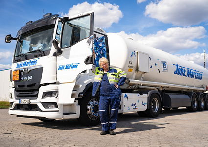 a truck driver stands confidently in front of a white MAN tanker truck