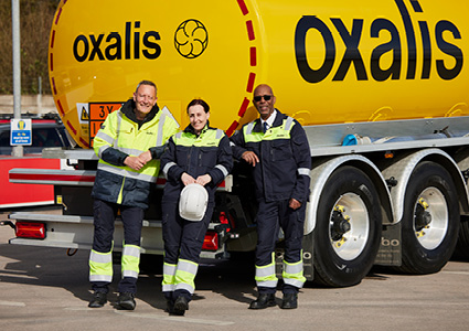 three employees of Oxalis Logistics posing in front of a large, yellow fuel tanker