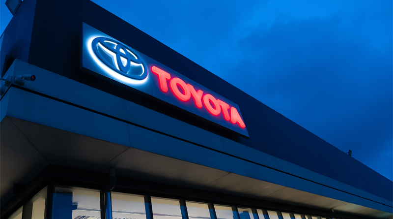 Illuminated Toyota dealership sign on the exterior of a modern showroom at dusk, representing the automaker's North American operations amid shifting production strategies.