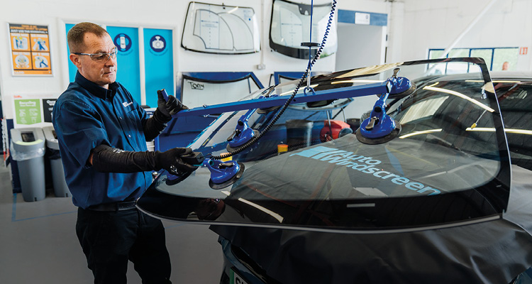 a technician carefully installing a new car windscreen using a specialized suction cup lifting tool