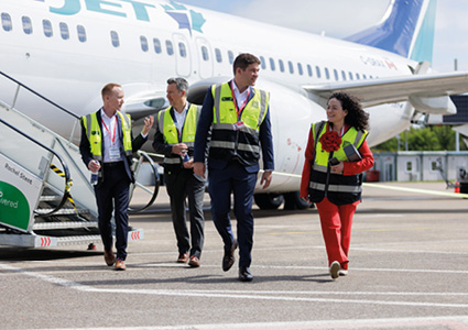 four people walking across an airport tarmac next to a large commercial airplane
