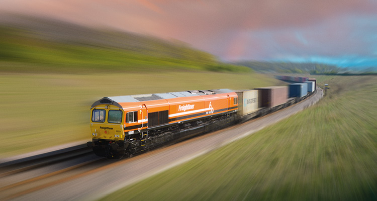 a Freightliner Class 66 diesel locomotive hauling an intermodal freight train along a rural route