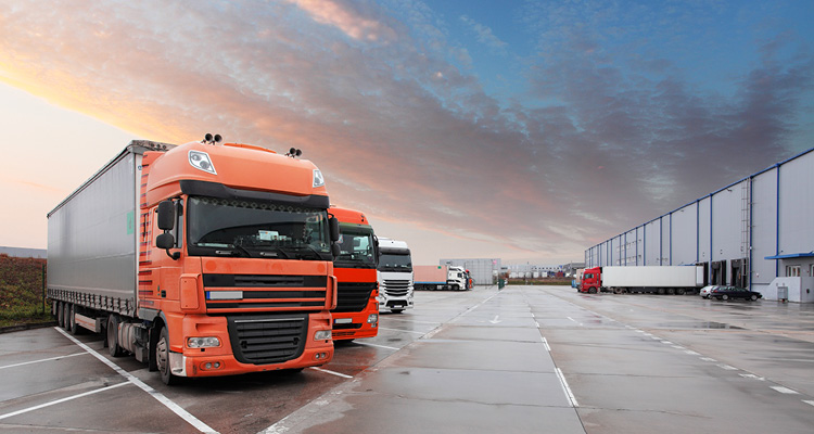large orange semi-truck parked in a paved logistics yard next to a warehouse