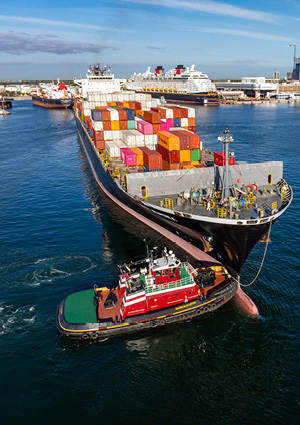 a red and green harbor tugboat assisting a large container