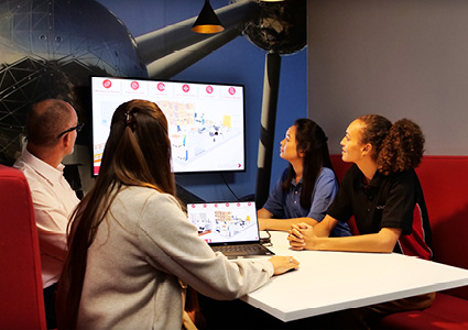 a group of people collaborating around a table with a laptop and a large monitor in an office