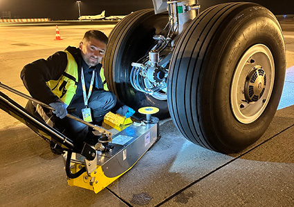 an aviation maintenance technician using a specialized hydraulic axle jack or wheel-change dolly to service the main landing gear wheel of a large commercial aircraft
