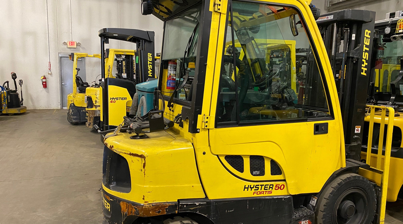 Yellow Hyster forklift inside an industrial warehouse alongside other material handling equipment.